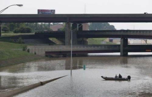 A boat is seen in flooded water along the I-75 roadway with the I-696 interchange bridges in the background.