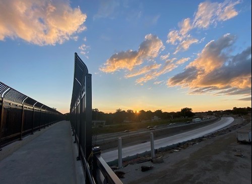 Sun setting in background with pedestrian walkway on the left and reconstructed roadway on the right